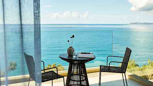 Balkong med havsutsikt, bord med vase og to stoler. (AI-generert tekst)