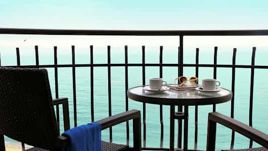 Balkong med bord og stoler som vender mot havet. (AI-generert tekst)