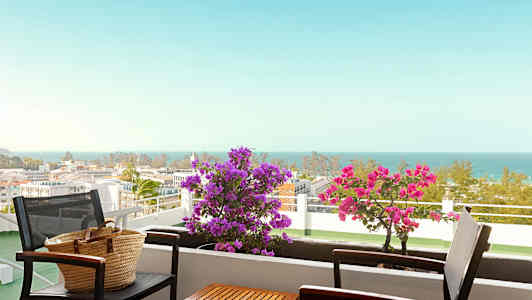 En balkong med bord og stoler, blomster og havutsikt. (AI-generert tekst)