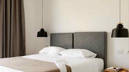 Hotellrom med grå sengegavl, hvit seng og to svarte hengende lamper. (AI-generert tekst)