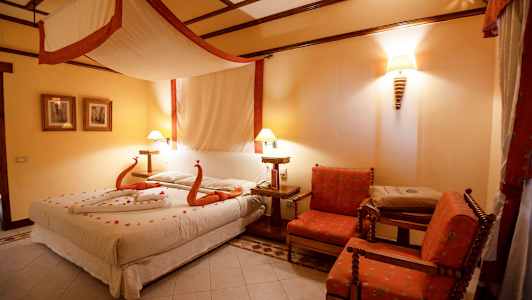 Et hotellrom med en stor seng dekorert med håndklær formet som svaner og blomster, to stoler og et bord. (AI-generert tekst)