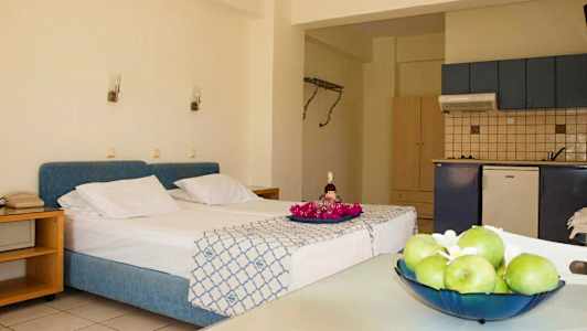 Rommet har en seng med blå sengegavl, et kjøkken og et bord med frukt. (AI-generert tekst)