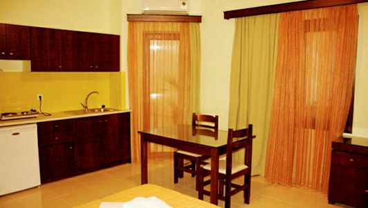 Et rom med et kjøkken, bord og to stoler samt gardiner ved vinduene. (AI-generert tekst)