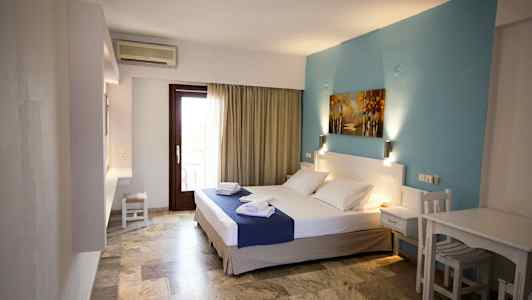 Et hotellrom med en dobbeltseng, blå veggdekorasjon og et bord med stoler. (AI-generert tekst)