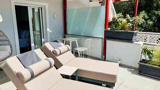 Terrasse med to solsenger og et bord med to stoler under en pergola. (AI-generert tekst)