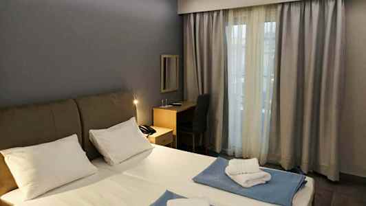 Et hotellrom med en dobbeltseng, skrivebord og et vindu med gardiner. (AI-generert tekst)