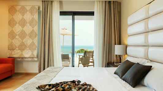 Hotellrom med seng og havutsikt fra en møblert terrasse. (AI-generert tekst)