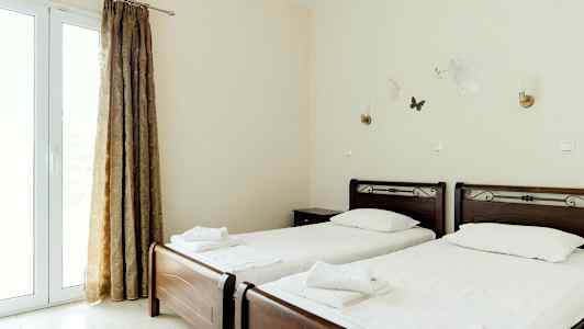 To enkeltsenger med hvitt sengetøy og mørke tresengegavler, i et lyst rom med gardiner og veggdekorasjoner. (AI-generert tekst)