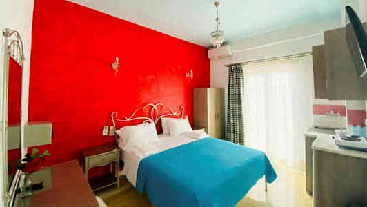 Et hotellrom med en dobbeltseng, rød veggdel og lyseblåt sengeteppe. (AI-generert tekst)