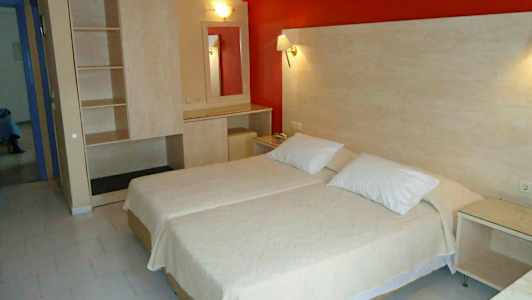 Et hotellrom med to enkeltsenger ved siden av hverandre, et skap og et bord med speil. (AI-generert tekst)