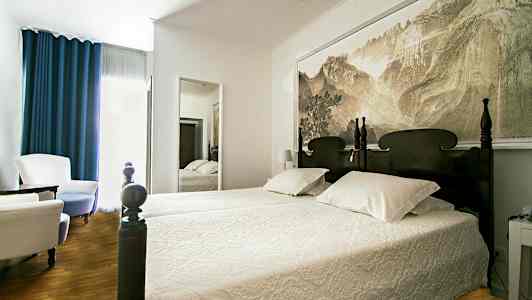 Seng med utskåret hodegjerde i et rom med veggspeil og sittemøbler. (AI-generert tekst)