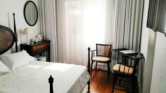 Et hotellrom med en seng, skrivebord og stol, samt et vindu med hvite gardiner. (AI-generert tekst)