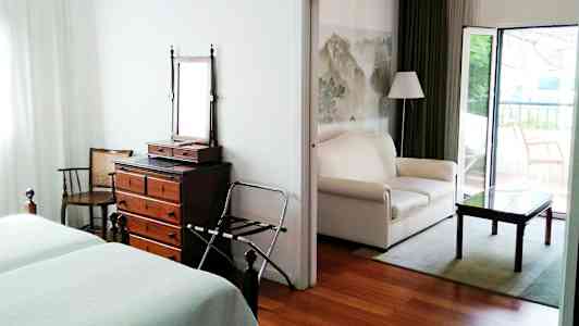 Et hotellrom med to senger, en kommode med speil og en åpen sittegruppe med sofa og bord. (AI-generert tekst)