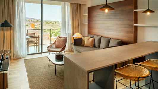 En moderne stue med sofa, lenestol og kjøkkenbar. Store vinduer vender mot en terrasse. (AI-generert tekst)