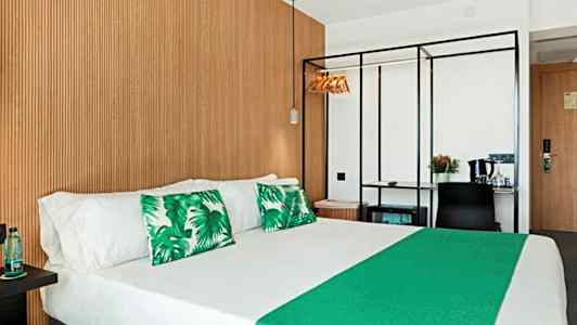 Hotellrom med dobbeltseng, grønne dekorasjonsputer og trepanel på veggen. (AI-generert tekst)