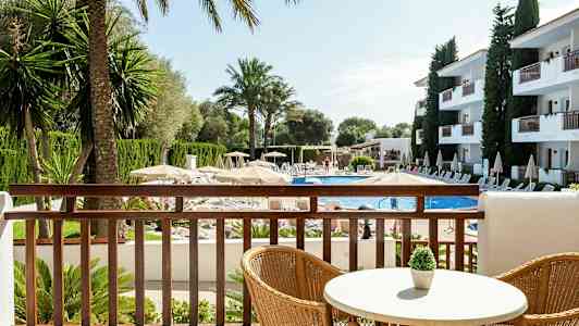 Utsikt fra en balkong over et basseng omgitt av solsenger, parasoller og bygninger. (AI-generert tekst)