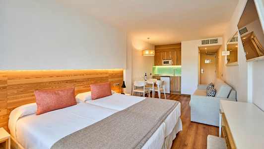 Innredning av et hotellrom med dobbeltseng, kjøkkenområde og sitteplass. (AI-generert tekst)