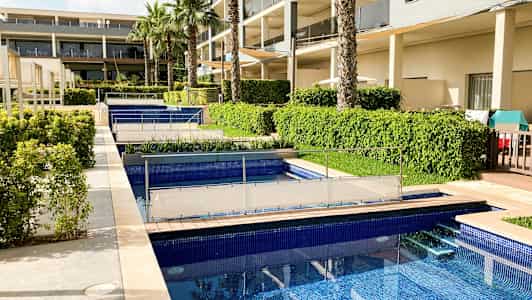 Et bilde av hotellområdet med flere bassenger, grønne busker og palmer nær bygningen. (AI-generert tekst)