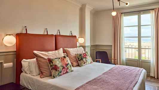 Et hotellrom med en seng, dekorative puter og et vindu som viser utsikt. (AI-generert tekst)