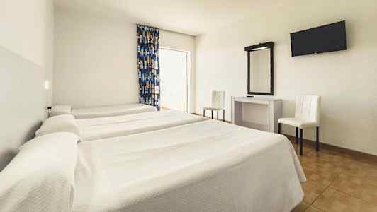 Et hotellrom med tre enkeltsenger, et skrivebord med speil, to stoler og en veggmontert TV. (AI-generert tekst)