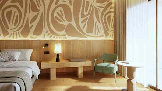 Bilde av et moderne hotellrom med dekorativ kunst på veggen. Det er en seng til venstre, et nattbord med en lampe, en grønn stol og et rundt bord nær et stort vindu. (AI-generert tekst)