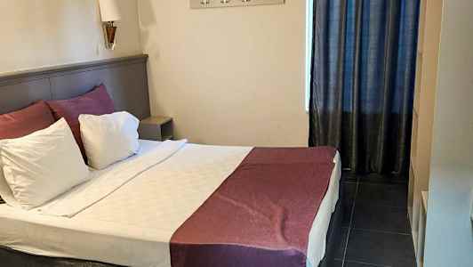 Et hotellrom med en oppredd dobbeltseng, en veggmontert knaggrekke og mørke gardiner. (AI-generert tekst)