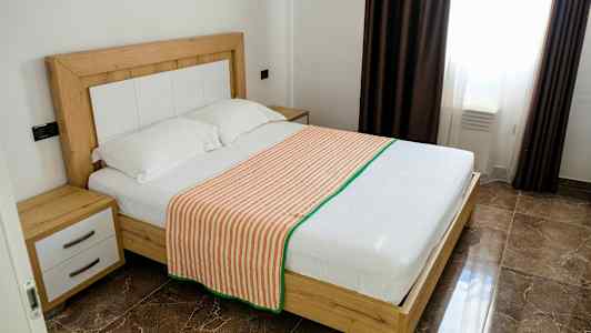 Et soverom med en dobbeltseng med treramme, to puter og et stripete sengeteppe. (AI-generert tekst)