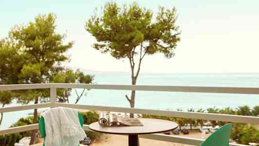 En balkong med grønne stoler, et bord og utsikt over trærne og havet. (AI-generert tekst)