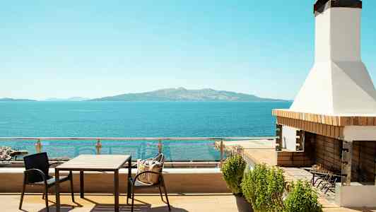 En terrasse med bord, stoler og grill med utsikt over havet og en fjern øy. (AI-generert tekst)