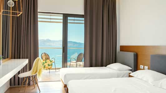 Hotellrom med to enkeltsenger og tilgang til en balkong med utsikt over havet. (AI-generert tekst)