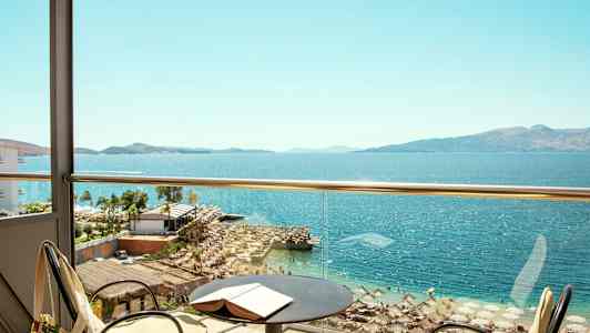 Utsikt fra en balkong mot en strand og hav med parasoller og solsenger. (AI-generert tekst)