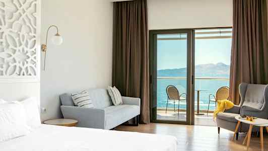 Hotellrom med seng, sofa, lenestol og balkong med havutsikt. (AI-generert tekst)