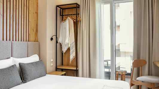 Et rom med en seng, en stol og en åpen klesstativ nær et vindu. (AI-generert tekst)