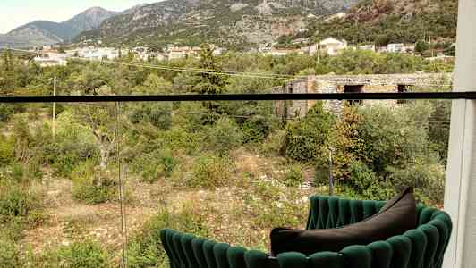 Utsikt fra balkongen mot en grønn dal med trær, busker og bygninger i bakgrunnen. (AI-generert tekst)