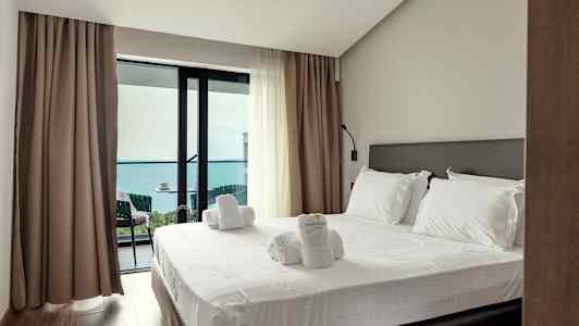 Et hotellrom med en oppredd seng og utgang til en balkong med havutsikt. (AI-generert tekst)