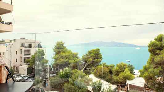 Utsikt fra en balkong mot havet og grønne trær. (AI-generert tekst)