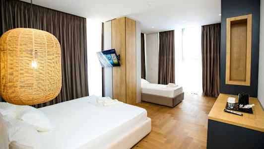 Et hotellrom med to senger, en hengende lampe, en veggmontert TV og et skrivebord med en kaffetrakter. (AI-generert tekst)