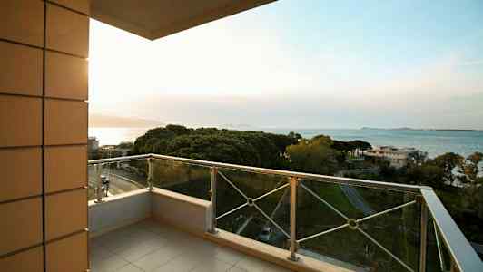 En balkong med glassrekkverk og utsikt over havet og grønne områder. (AI-generert tekst)