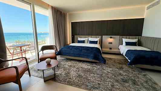 Et hotellrom med to senger og en balkong med havutsikt. (AI-generert tekst)