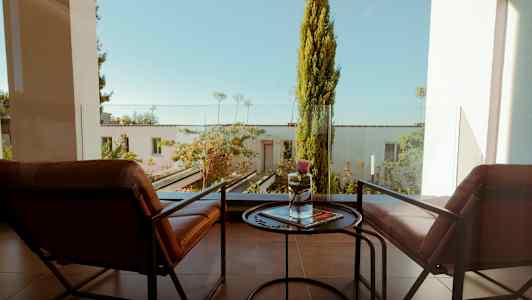 To stoler og et lite bord på en balkong med utsikt over en frodig hage. (AI-generert tekst)