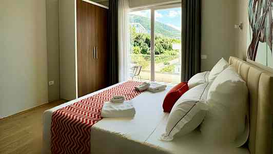 Et hotellrom med en seng, dekorert med røde puter og sengeteppe, samt utsikt mot et frodig landskap fra vinduet. (AI-generert tekst)