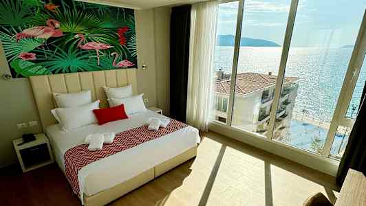 Soverom med stor seng, flamingomotiv på veggen og havutsikt gjennom panoramavinduer. (AI-generert tekst)