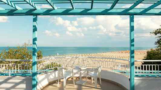 Utsikt mot stranden og havet fra en terrasse med sittemøbler. (AI-generert tekst)