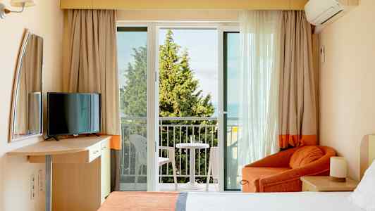 Et hotellrom med balkong, seng, lenestol og TV. (AI-generert tekst)