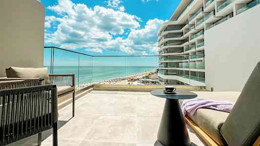 Utsikt fra en terrasse mot havet og en del av en bygning med moderne design. (AI-generert tekst)