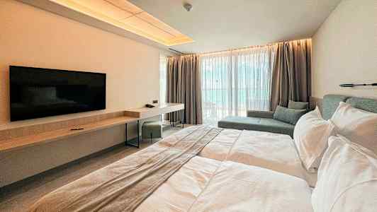 Et moderne hotellrom med en dobbeltseng, veggmontert TV, skrivebord og sitteområde ved store vinduer. (AI-generert tekst)