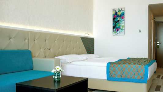 Et moderne hotellrom med en dobbeltseng, turkis sofa og veggkunst. (AI-generert tekst)