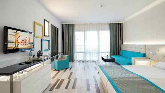 Et hotellrom med en seng, en sittegruppe, et skrivebord og en balkong. (AI-generert tekst)