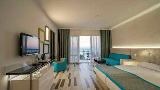 Interiør av et hotellrom med en seng, sofa og utsikt mot en balkong. (AI-generert tekst)