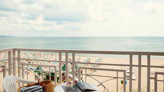 Utsikt fra balkong mot en strand med parasoller og solsenger samt havet i bakgrunnen. (AI-generert tekst)